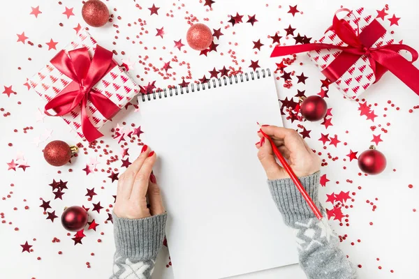 Mujer con suéter gris escribiendo una lista de planes y sueños para el próximo año. Lista de deseos para Navidad. Lista de tareas para Nuevo 2020 año con la decoración roja de vacaciones . —  Fotos de Stock