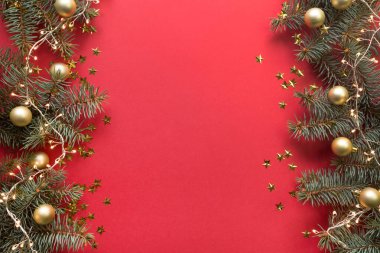 Noel çerçevesinde köknar dalları, altın toplar, kırmızı arka planda çelenkler. Metin için boşluk, yukarıdan görünüm, düz yatış. Mutlu yıllar..