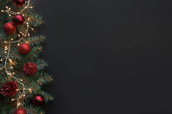 Noel çerçevesinde köknar dalları, kırmızı toplar, siyah arka planda çelenkler. Metin için boşluk, yukarıdan görünüm, düz yatış.