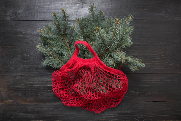 Vacaciones sin residuos de Navidad. Ramas de abeto de coníferas en bolso ecológico de algodón rojo sobre tabla de madera negra. Eco amigable Navidad . — Foto de Stock