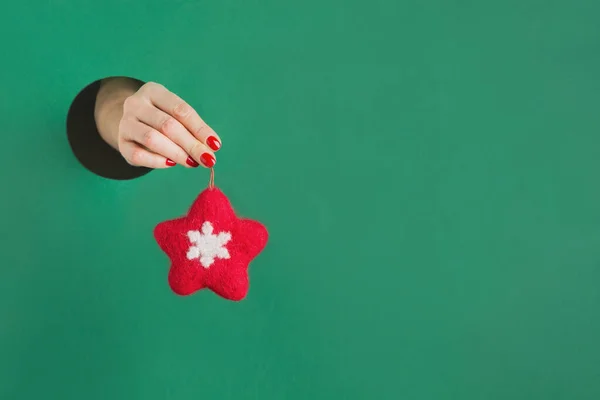 Mano femminile tenuta feltro stella rossa attraverso foro rotondo in carta verde. Giocattolo fatto a mano. Arredo natalizio . — Foto Stock