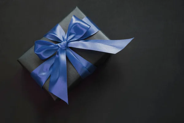 Caixa de presente embrulhada em papel preto com fita azul clássica na superfície preta . — Fotografia de Stock