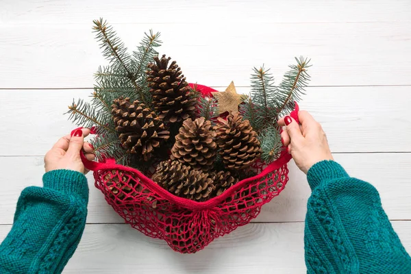 Woman hands holding mesh bag with Christmas zero waste decor, natural cones for handmade gifts and DIY.