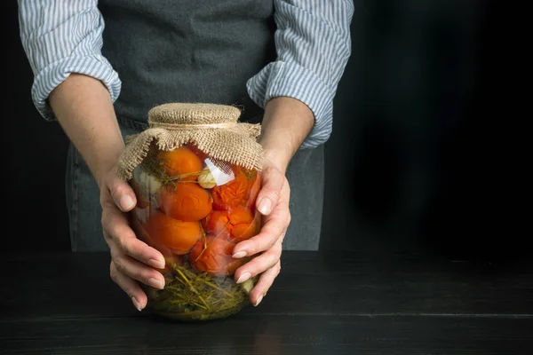 Tomates marinados caseros. Mujer sosteniendo verduras enlatadas en frascos de vidrio sobre tabla de madera. Espacio para texto . — Foto de Stock