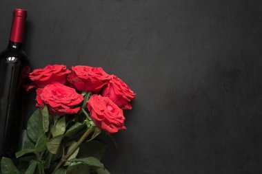 Bir buket romantik kırmızı gül, siyah masada bir şişe kırmızı şarap. Boşluğu olan üst görünüm.
