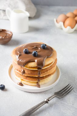 Sweet homemade stack of pancakes with chocolate and blueberry on white table.