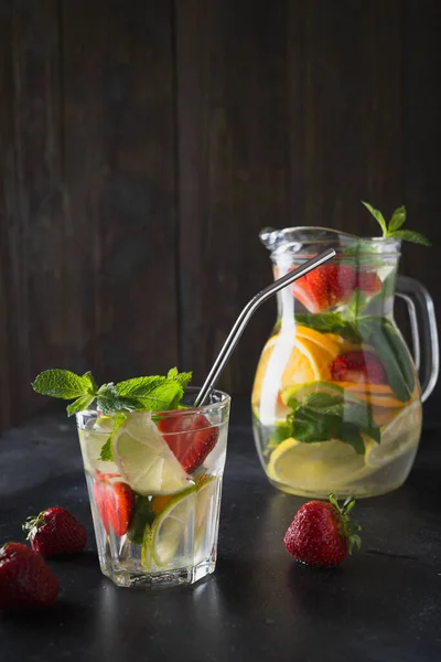 排毒柠檬水与石灰,橙子,柠檬,草莓在玻璃和罐子。夏季健康新鲜饮料。深色木制背景. — 图库照片