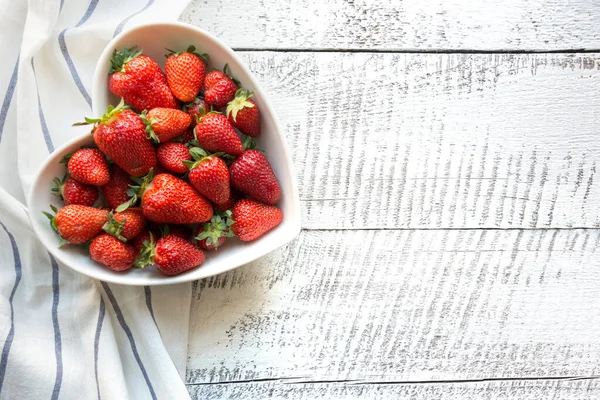 将成熟的有机草莓放在盘子里，作为心脏放在白色木制背板上 — 图库照片