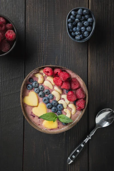 Batido de plátano y arándanos con frutas decoradas en cuenco de coco sobre tabla de madera. Comida limpia, comida vegetariana. Formato vertical . — Foto de Stock