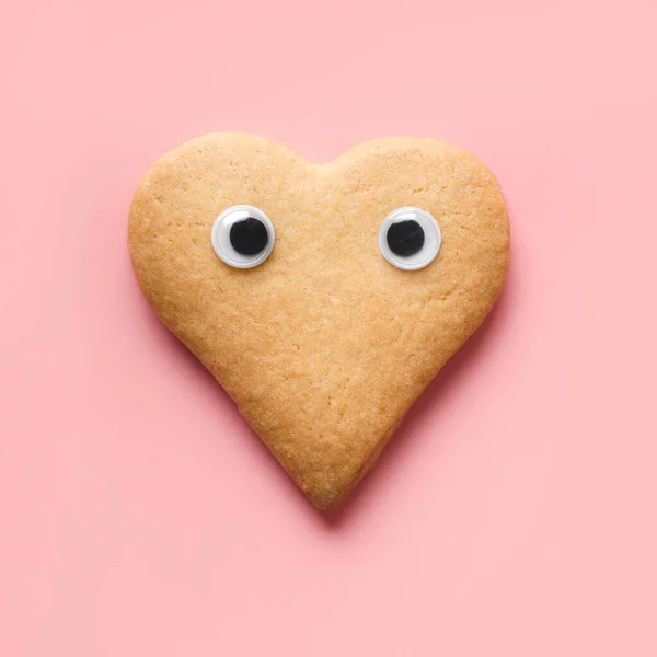 Biscotti a forma di cuore con occhi durante il giorno di San Valentino su rosa. Concetto di cibo. Vista dall'alto . — Foto Stock