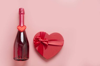 Sevgililer Günü tebrik kartı. Bir şişe köpüklü şarap, hediye kutusu şeklinde kalp ve pembe kurdele. Üst Manzara. Metin için boşluk.