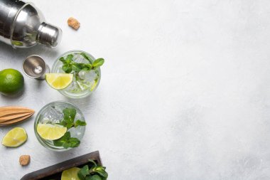 Mojito kokteyl malzemeleri, limon, nane şekeri, karıştırıcı, gri ışıklı masa üzerindeki jigger. Yukarıdan bak. Yatay format. Metin için boşluk.