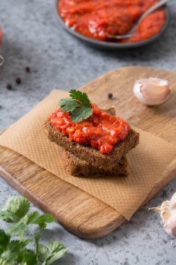 Bir dilim çavdar ekmeği ve ev yapımı makarna ayvar. Sebze sosu mu yoksa grinin üzerine fırında kırmızı dolma biber havyarı mı? Balkan aperatifleri mutfağı. Dikey format. Kapat..