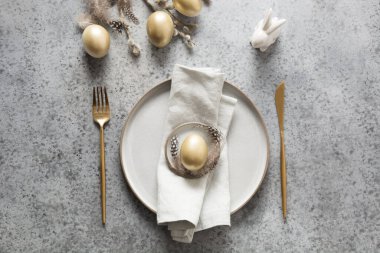 Elegant Easter table setting with golden eggs and bunny on grey stone table. Top view. clipart