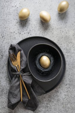 Easter table setting with black and golden decor on grey stone table. Top view. Vertical format. Minimal composition with nest. clipart