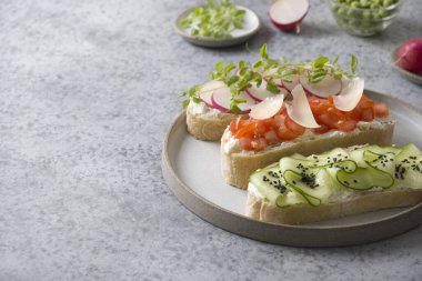 Ciabatta tostunda üç sandviç, taze sebzeler, turplar, domatesler, salatalıklar ve gri arka planda mikroyeşiller. Kapatın. Boşluğu kopyala.