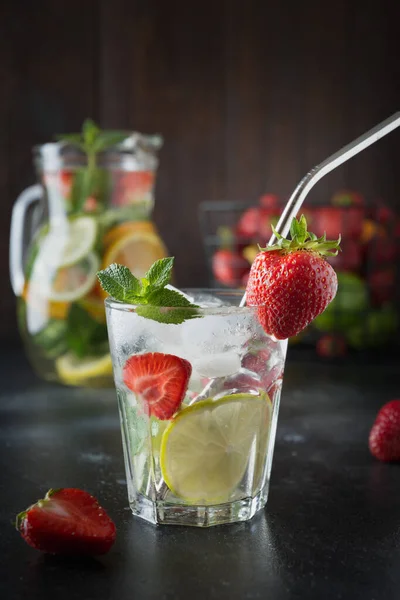 排毒柠檬水与石灰 草莓在玻璃和壶 夏季健康新鲜饮料 垂直方向 深色木制背景 — 图库照片