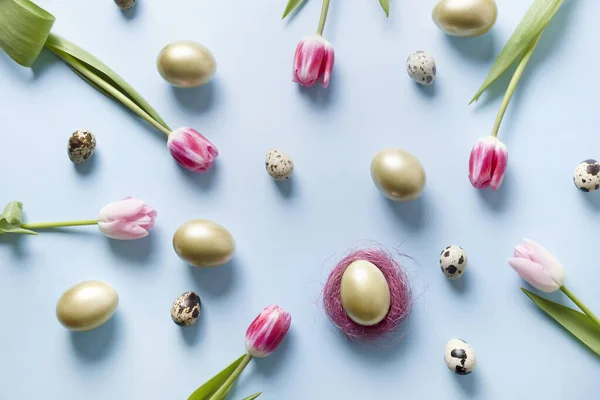 Composición de Pascua de tulipanes rosados, huevos dorados y conejito en azul pastel. Vista superior . — Foto de Stock