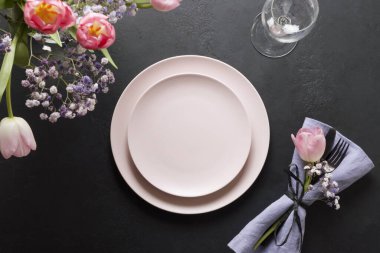 Taze pembe laleler ve siyah taş masanın üzerinde pembe dekoru olan bir bahar masası. Üst Manzara. Zarif bir akşam yemeği..