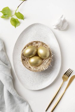Beyaz masada tavşanlı ve altın yumurtalı Paskalya sofrası. Yukarıdan bak. Dikey biçim.