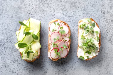 Sandwiches with sundries tomatoes, fresh radish, microgreens, cream cheese on grey background. Top view. clipart