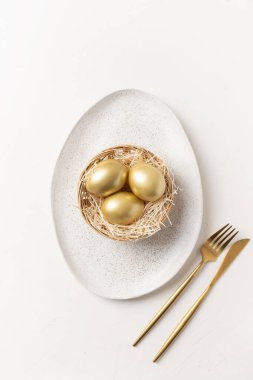 Yuvasında altın yumurtalar olan Paskalya sofrası beyaz masada. Yukarıdan bak. Dikey biçim.
