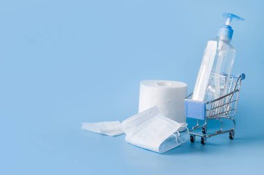 Dezenfekte jeli, ıslak mendilli, koruyucu maskeli market arabası. Coronavirus salgını sırasında alışveriş yapma tehlikesi kavramı COVID-19. Az mal ve temel ilaçlar.