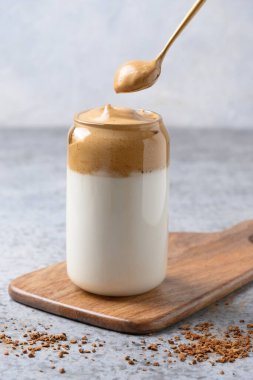 Bardakta Dalgona kahvesi ve gri kaşık. Kore kahveli latte espresso köpüklü hazır kahve. Dikey çekim.