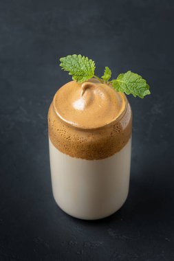 Dalgona köpüklü kahve, cam kaplı Melissa 'yı siyah üzerine garnitür. Trend Koreliler hazır kahveyle soğuk süt içerler. Dikey çekim.
