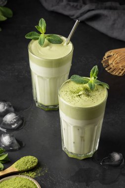 İki bardak Dalgona Buzlu Matcha çayı. Siyah arka planda beyaz yumurtalı soğuk süt ve çırpılmış kibrit çayı. Zamanda kendini izole eden enfes viral içecekler. Dikey biçim.