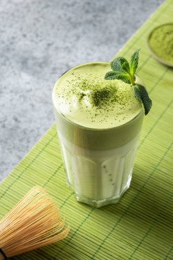 Bir bardak Dalgona Buzlu Matcha çayı. Çayla çırpılmış beyaz yumurta buzlu süte eklenir. Dikey biçim.