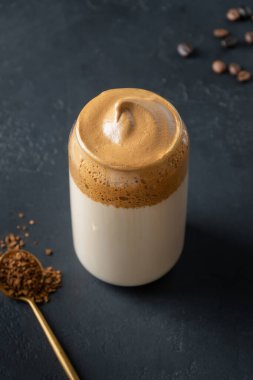 Dalgona köpüklü, siyah bardakta kahve. Hazır kahve köpüklü Kore buzlu latte içeceği. Dikey çekim.