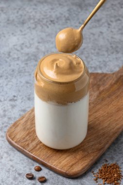 Bardakta Dalgona kahvesi ve gri kaşık. Kore kahveli latte espresso köpüklü hazır kahve. Dikey çekim.