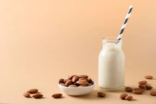 Fresh almond milk in glass bottle and almonds around on beige background. Close up. Space for text. Healthy vegan milk replacer. Lack of cholesterol.