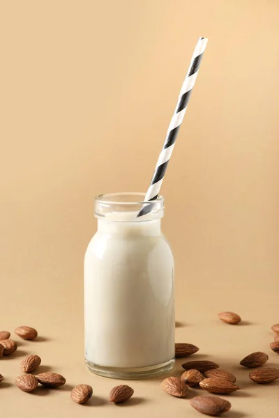 Fresh almond milk in glass bottle and almonds around on beige background. Close up. Vertical format. Healthy vegan eating. Lack of cholesterol.