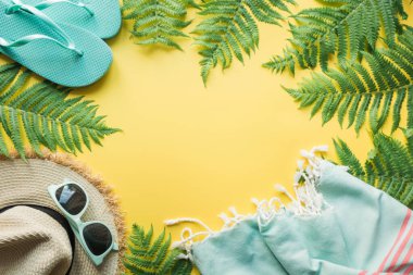 Plajdaki kadın aksesuarlarının sınırı. Tropik tatiller, hasır güneş şapkası, havlu, eğreltiotu yaprakları sarıda. Yaz kavramı. Metin için boşluk olan üst görünüm.