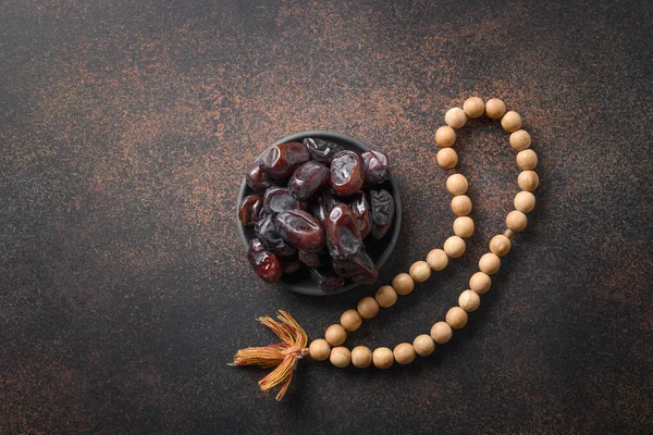 Ramadan. Wooden prayer beads and dates in bowl on brown. View from above. Eid Mubarak. Religious tradition.