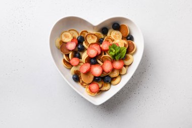 Beyaz arka planda kalp şeklinde yaban mersini ve çilekli gözlemeler. Yukarıdan görüntüle.