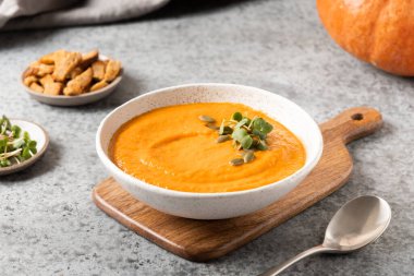 Gri arka planda kremalı garnitürlü balkabağı çorbası. Kapat..