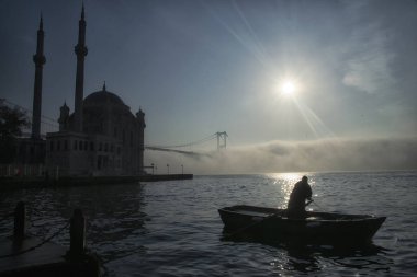İstanbul 'un sisli sabahında Boğaz Köprüsü, Ortakoy Camii ve Balıkçı