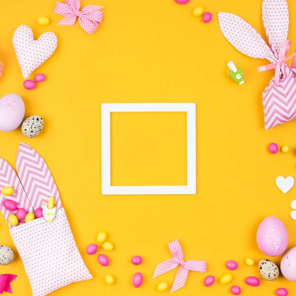 Keret az üzenetet a húsvéti dekoráció: tojás, nyuszi zsák és a cukorkát a sárga háttér — Stock Fotó