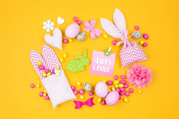 Easter decoration with eggs, bunny bag and candy on yellow background — Stock Photo, Image