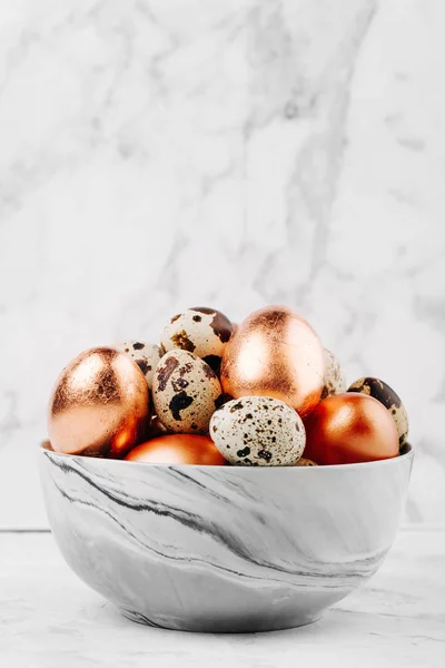 Bowl with painted bronze and quail  Easter eggs on a marble background.
