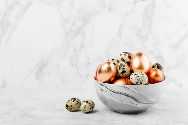 Mangkuk dengan dicat perunggu dan burung puyuh telur Paskah di latar marmer . — Stok Foto