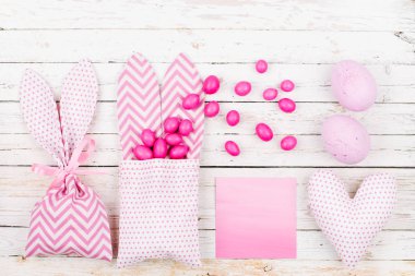 Bunny tedavi çanta pembe şeker, boş oyun kağıdı, yumurta ve kalp ile. Ahşap arka plan üzerinde Paskalya kavramı