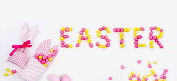 Schriftzug Ostern ist mit rosa und gelben Bonbons und Hasentüten auf weißem Hintergrund — Stockfoto