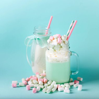 Şekerleme ve mavi bir arka plan üzerinde pembe kamış bir cam kavanoza bir nane shake süt