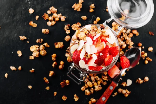 Healthy breakfast, berry smoothie in a glass jar topped with strawberry, almond flakes and granola on black background — Stock Photo, Image