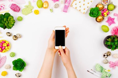 Bir akıllı telefon tutarak el. Paskalya dekorasyonu ile çalışma alanı. Düz yatıyordu, en iyi görünümü