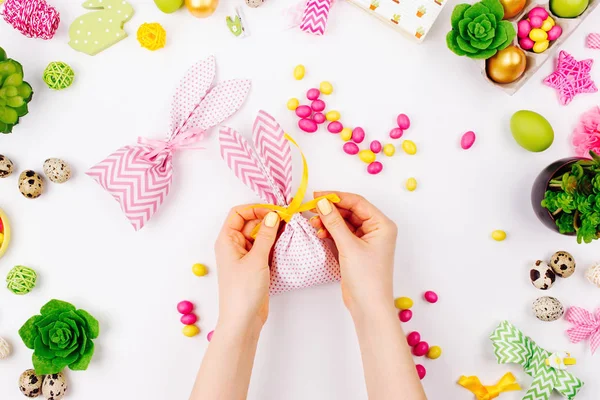 Mujer envuelve golosinas en bolsas de regalo de conejito de tela. Concepto de Pascua. Piso tendido, vista superior — Foto de Stock